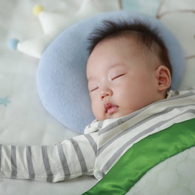 petit bébé qui dors avec sa tête sur un oreiller bleu