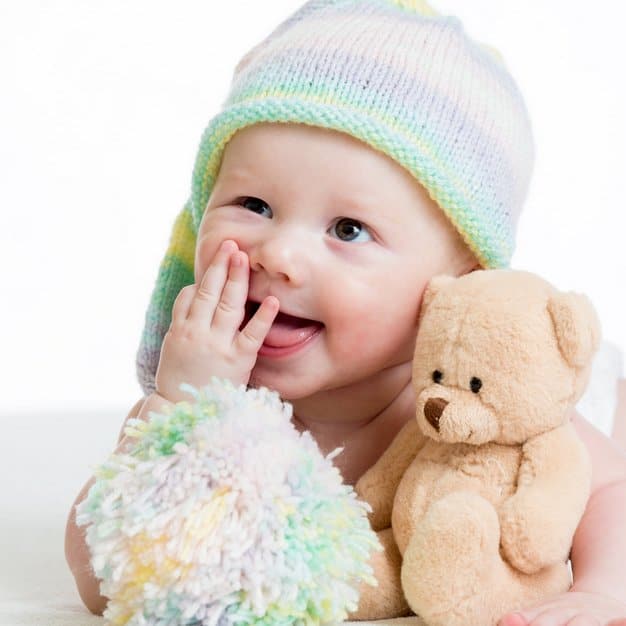 bébé qui porte un bonnet et tient son doudou un ours en peluche