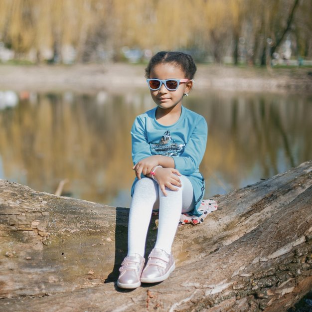 Petite fille assise dans un park portant des lunettes de soleil