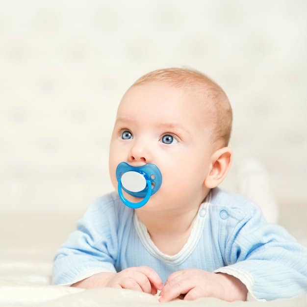 petit bébé avec une tétine blanche et bleue qui regarde devant lui