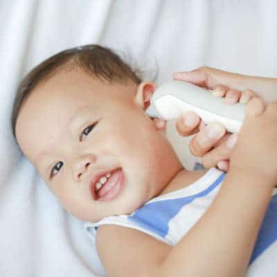 Un bébé qui sourit et qui se fait prendre sa température avec un thermomètre numérique