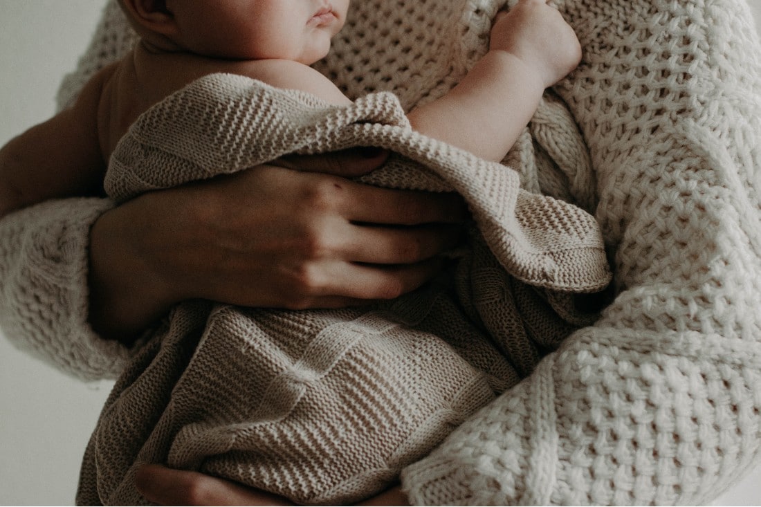 Baby in Mamas Armen, eingewickelt in eine Decke