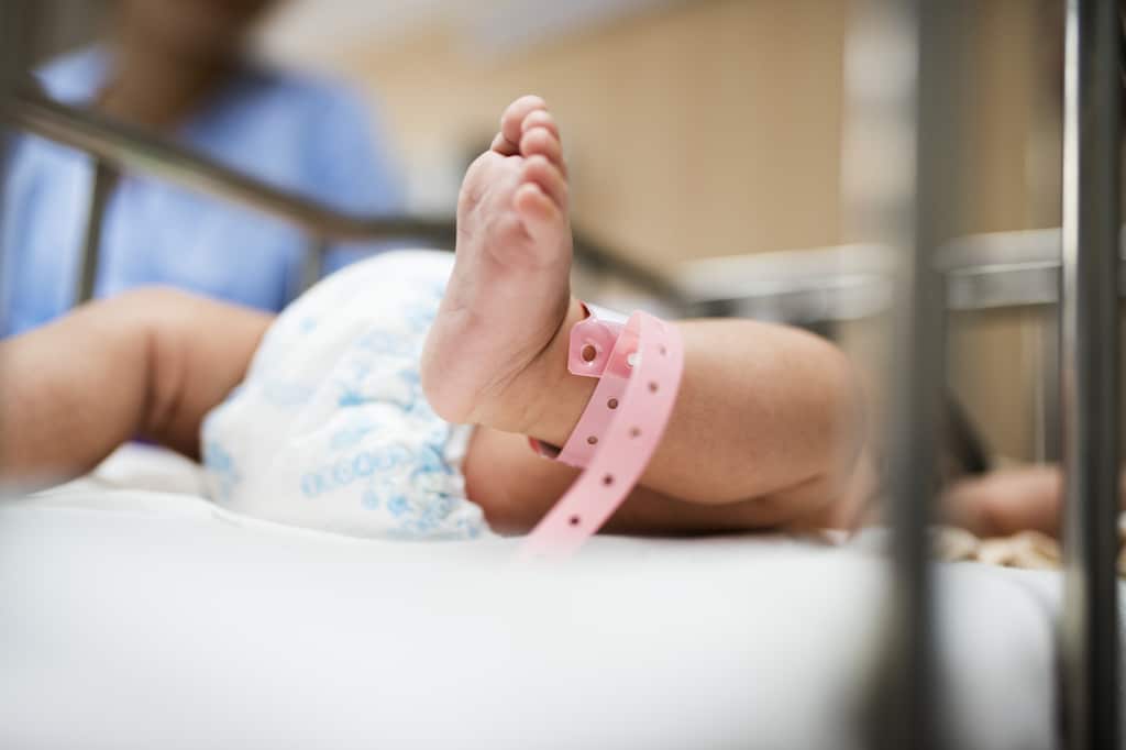 ein Baby liegt in seinem Bettchen im Krankenhaus mit Blick auf seine Beine und das um seinen Knöchel gewickelte Armband