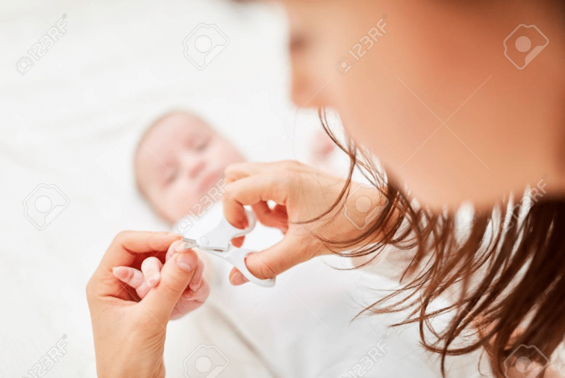 ein liegendes Baby mit ausgestreckter Hand, das von seiner Mutter gehalten wird, die seine Nägel mit einer runden Schere schneidet