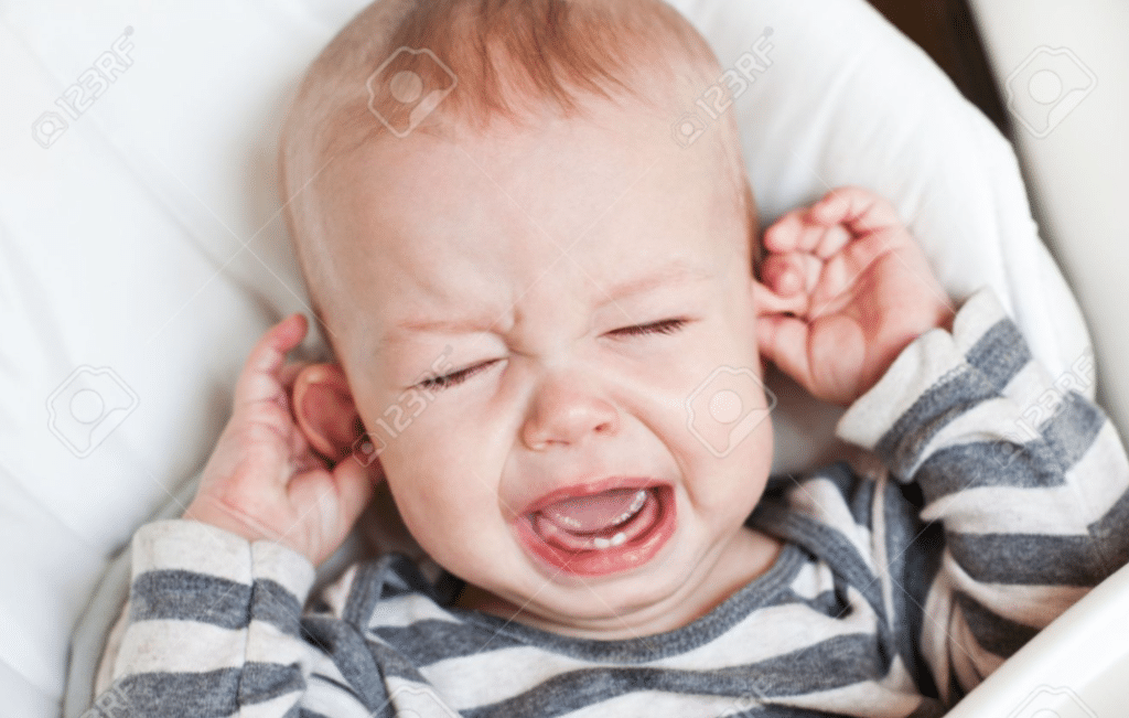 ein Baby schreit in seinem Stubenwagen und hat den Mund weit aufgerissen, die Augen geschlossen und die Ohren angelegt