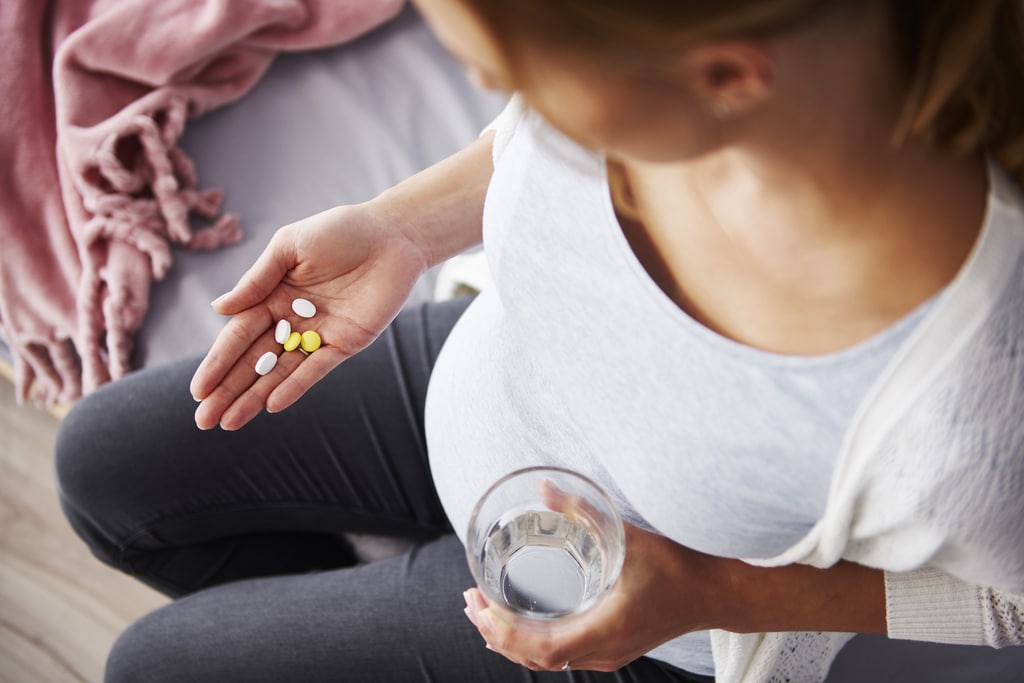 eine schwangere Frau hält Tabletten in der Hand und ein Glas Wasser in der anderen