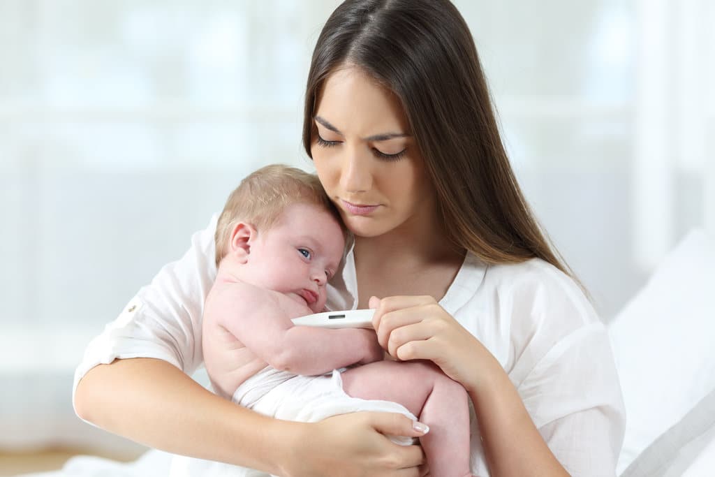 eine Mutter hält ihr Baby mit einem Thermometer
